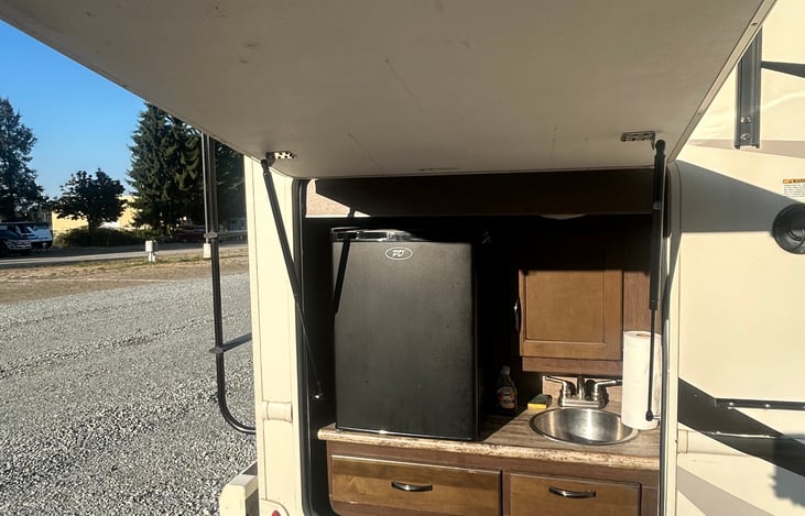The outdoor kitchen has a fridge, sink, and small cupboard.