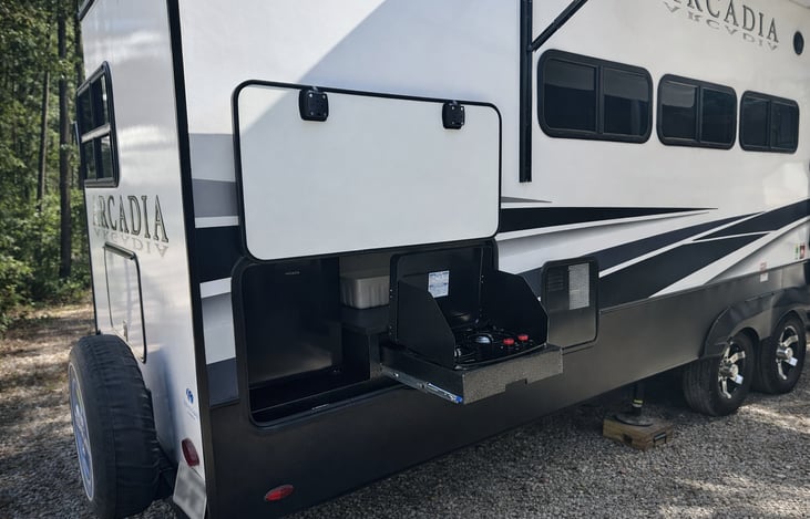 Exterior camp kitchen with propane oven, cooktop, and mini fridge. Cook meals outdoors while keeping drinks cold and easy to grab under the awning.