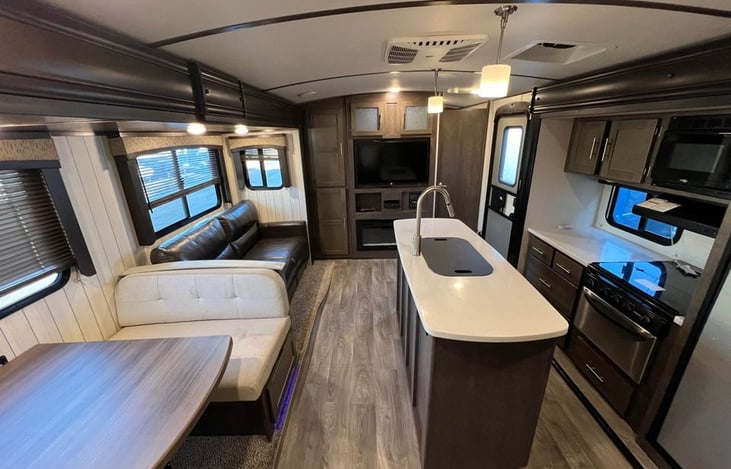 Open-concept interior with island kitchen, leather couch, large dinette, and LED lighting. Clean, spacious, and ready for good times.