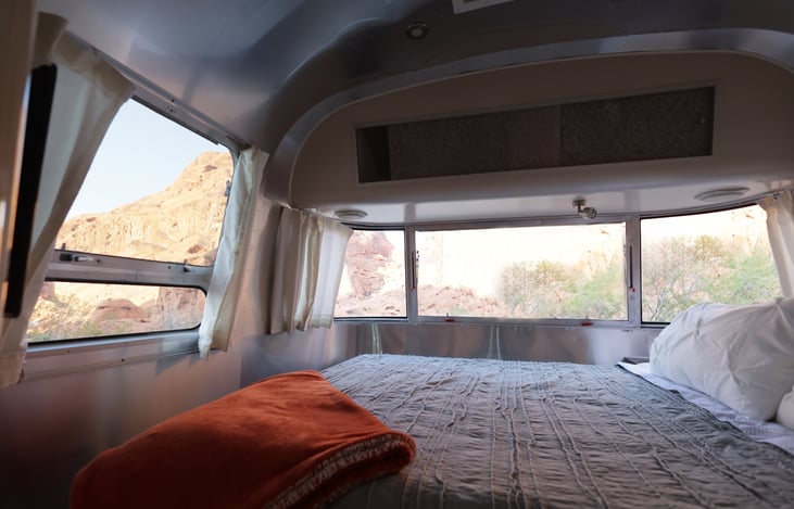 Walk around queen bed in the rear, with windows providing views on three sides. Bedroom also features an upper storage cabinet, wardrobe, storage under the bed, a second TV, and reading lights.