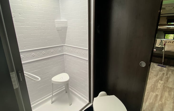 roomy shower with a sliding door and a shower stool.
