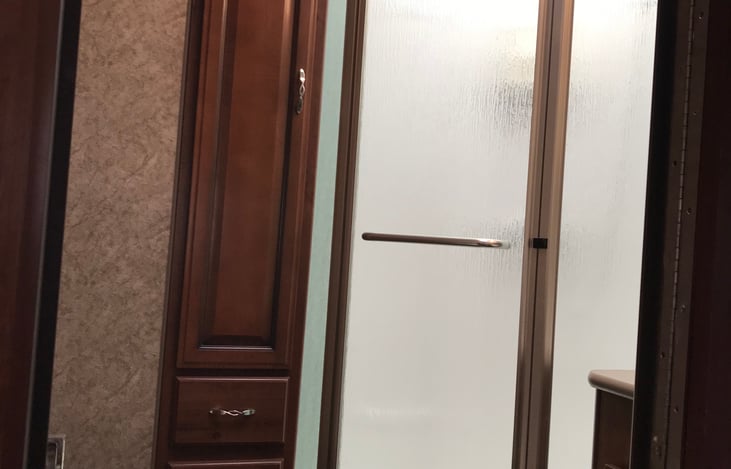 Corner shower with glass door with 3 drawer and cabinet storage.