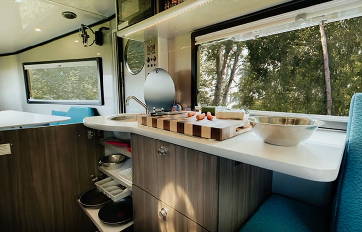 Kitchen with under-sink cabinet and pull-out shelves. Collapsable sink cover is open and fold-out faucet is shown.