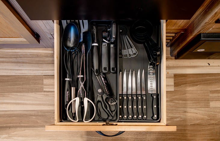 Kitchen drawer includes steak knives, cutting knife, measure cups, can opener, bottle opener, potato peeler, scissors, & cooking utensils. (Plates and utensils not included.)