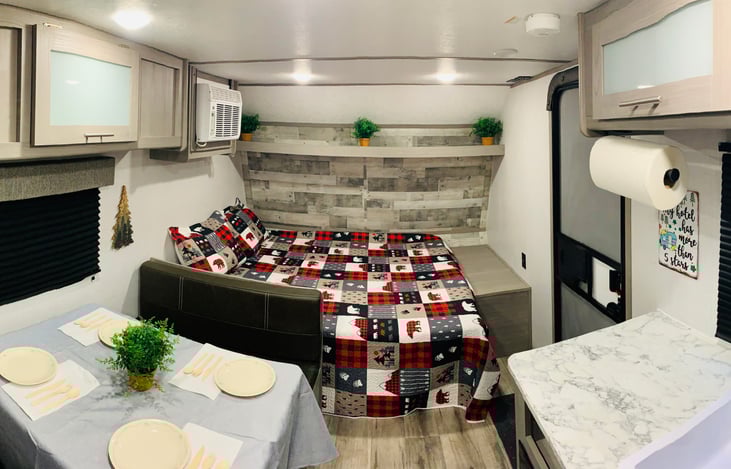 Panoramic Front-Half of Trailer showing setup Diner Table, Queen-Size Bed, Trailer Door, and Kitchen Area.