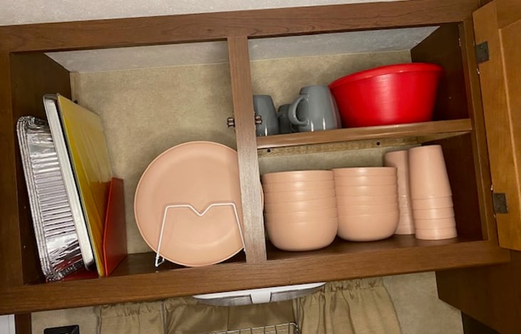 cabinet above kitchen sink, stocked with kitchen dishes , pans, cutting boards, nesting bowls and mugs