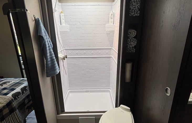 Bright shower with natural light coming from the skylight above. The shower has a retractable door and some perfectly placed shelves on the side for towels.