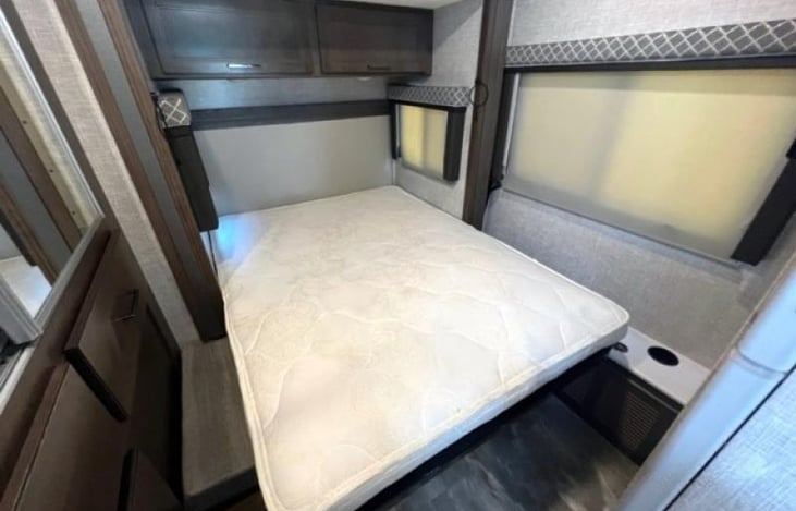 View of primary bed without the foam mattress topper or luxury linens. Storage cabinets above and below bed.