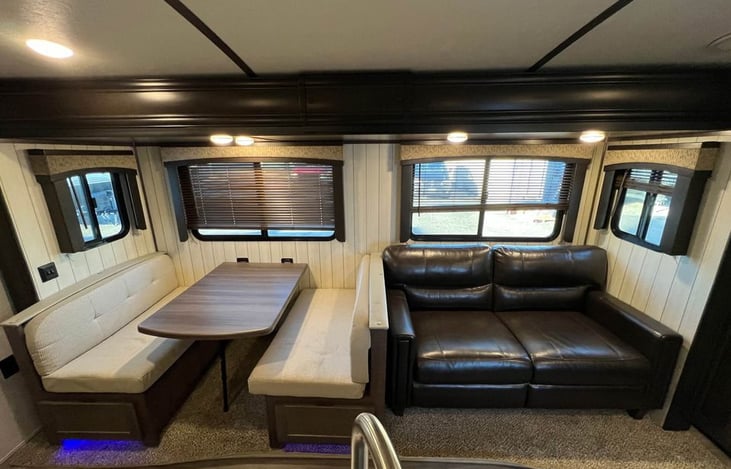 Spacious living area with wraparound dinette and leather sofa — both convert to extra sleeping space. Perfect for movie nights or rainy day hangouts.