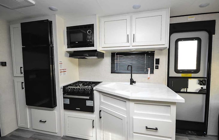 Spacious kitchen with 3 burner stove, conventional oven, microwave, medium size refrigerator, vent, silverware, pots/pans, plates/cups.