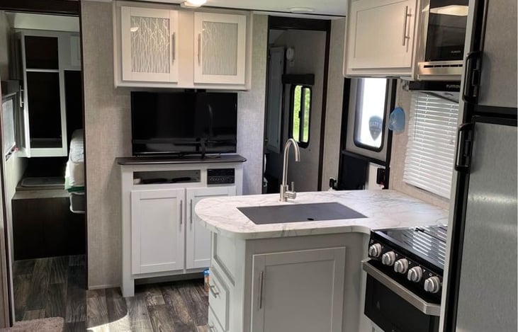 Queen bed behind TV. Kitchen with sink, stove and oven.