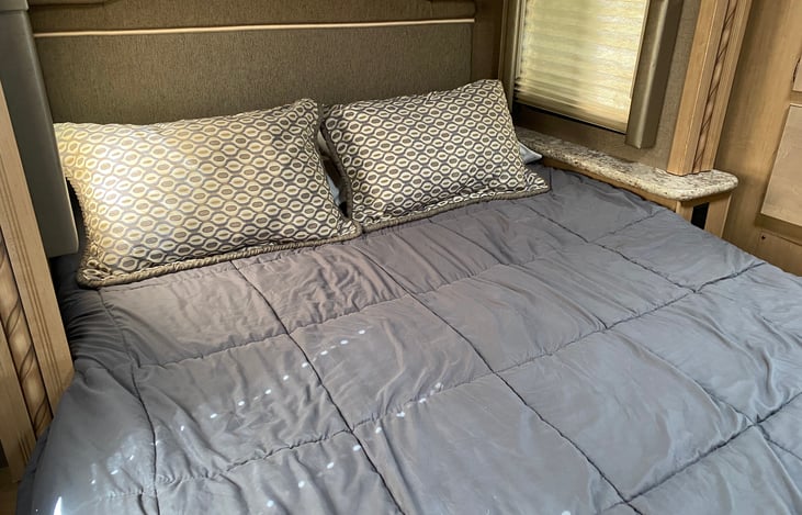 Comfortable queen-sized bunk in the rear of the vehicle. Plenty of overhead storage, and a single drawer to the side of the bed.  There's also a small television mounted to the wall opposite  the bed.
