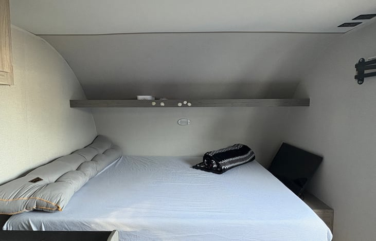 Brand-new main sleeping area featuring a comfortable mattress, extra pillows, and overhead storage.”