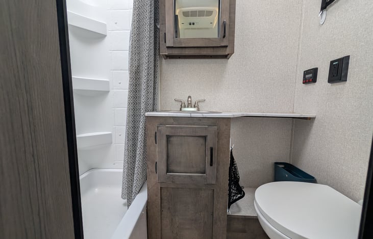 Full bathroom featuring a spacious walk-in shower with a overhead skylight for extra headroom, porcelain foot-flush toilet, vanity sink, and mirror with medicine cabinet storage.