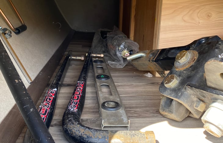 Left side of RV: Storage - hookup items including crank, pull bar, and bolt for adjusting hitch height