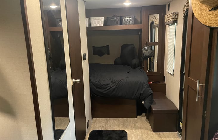 RV Queen bed with storage above and hanging closet to the side. Also another closet that can be used for clothes or as a pantry/supplies.