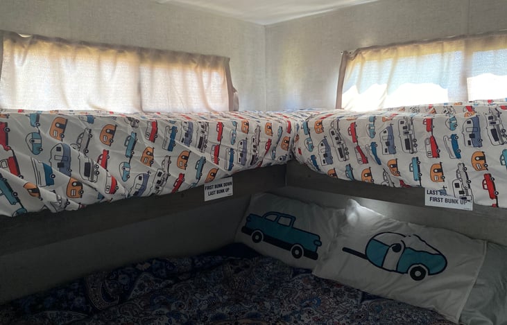 Two bunk beds down with sheets and the bottom queen bed with sheets down.