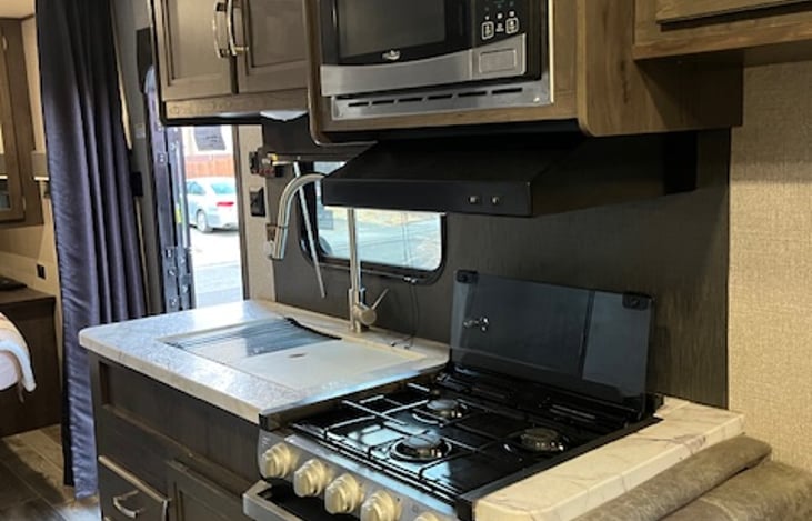 Kitchen includes 3 burner gas stove and oven, sink with hot and cold water, microwave with external venting and overhead light.
