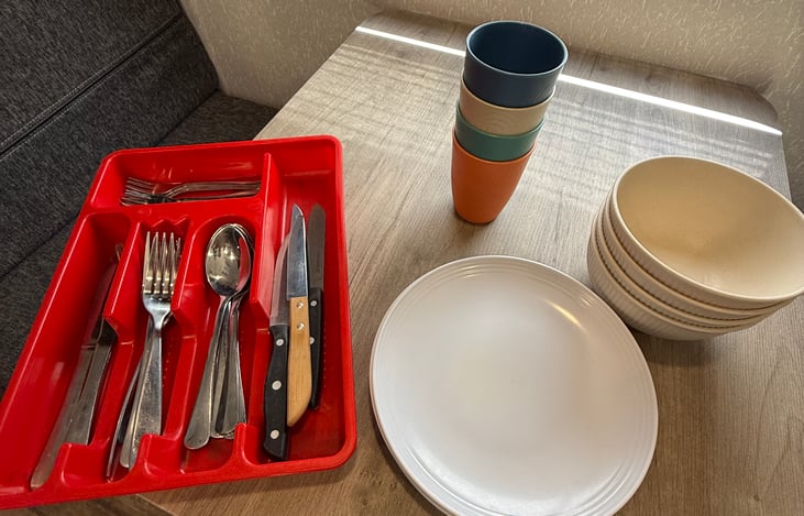 Tableware set up with 4 bowls, plates, and cups. Plus a whole set of silverware with knives