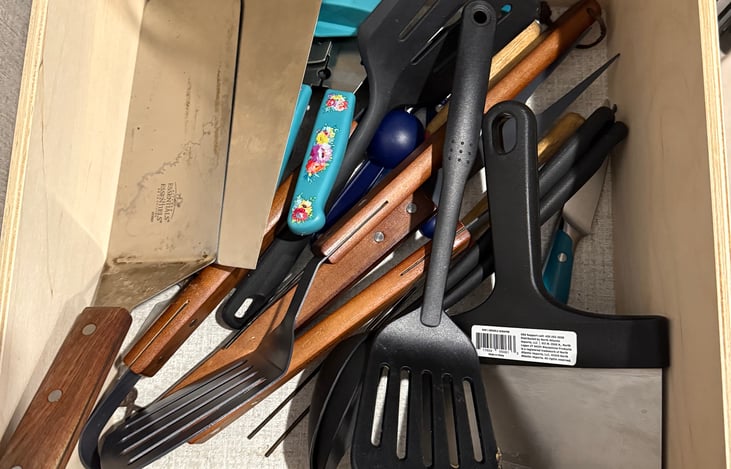 Kitchen drawers stocked with grilling utensils, cooking utensils, can opener, measuring cups, aluminum foil, straws, and matches.