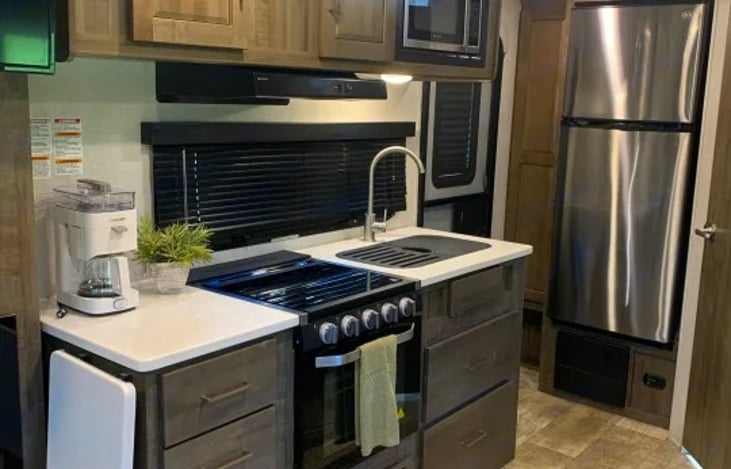 You will find solid-surface kitchen countertops, a flip-up extension, a stainless steel sink 10 cu. ft. refrigerator, 3 burner gas cooktop with a glass cover, a conventional gas oven & a microwave.