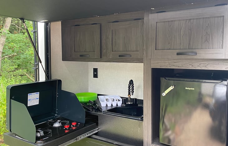 Outdoor kitchen equipped with mini fridge, sink, 2 burner gas stove, pots/pans/utensils, and storage space!