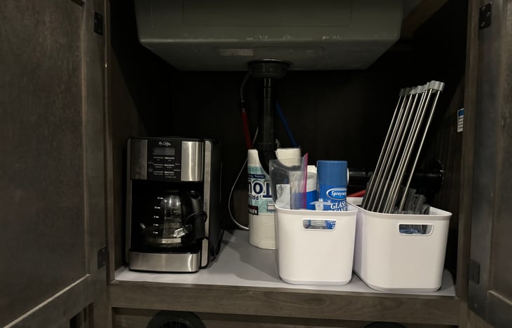 Below kitchen sink, drying rack, coffee pot and additional cleaning supplies.