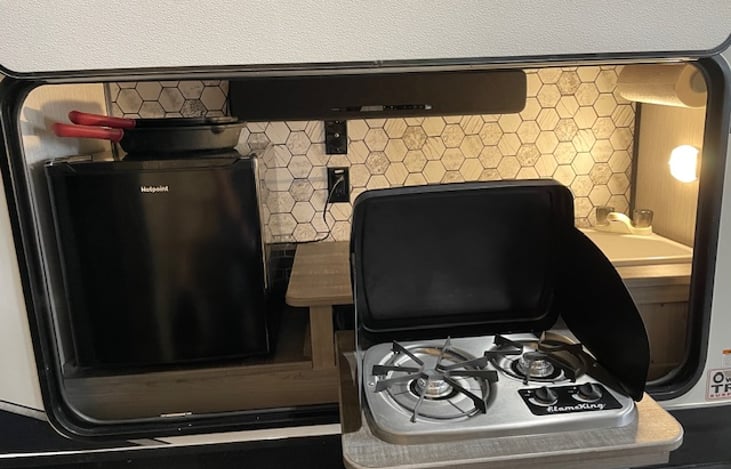 Outdoor kitchen with 2 burner gas cooktop, sink, sound bar, and mini fridge stocked with water!