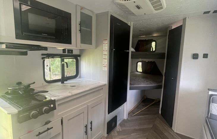 Kitchen includes 2-top gas burner, residential fridge, and microwave. Overhead cabinet includes coffee maker, drawer includes utensils, and cleaning supplies are available underneath the sink