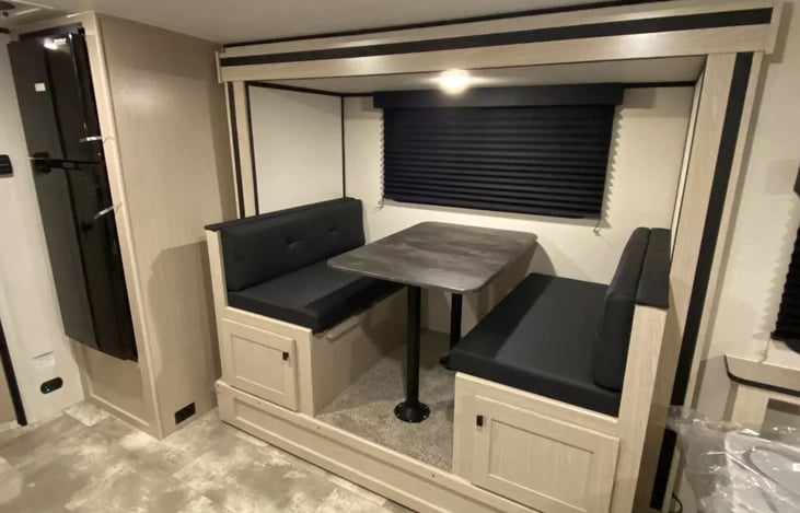 Dinette with pedestal table and under bench storage with easy access doors next to large refrigerator.  Dinette "folds down" into addition sleep area more suitable for smaller children.