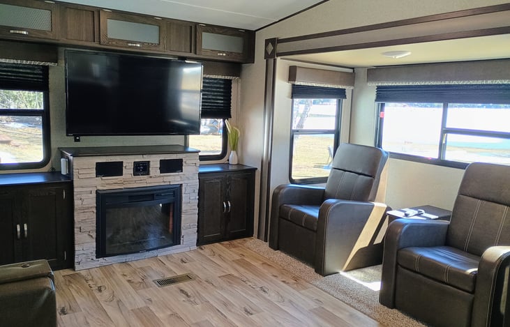 Smart TV and fireplace in the living room. Inside and outdoor speakers with radio. Also two reclining chairs.