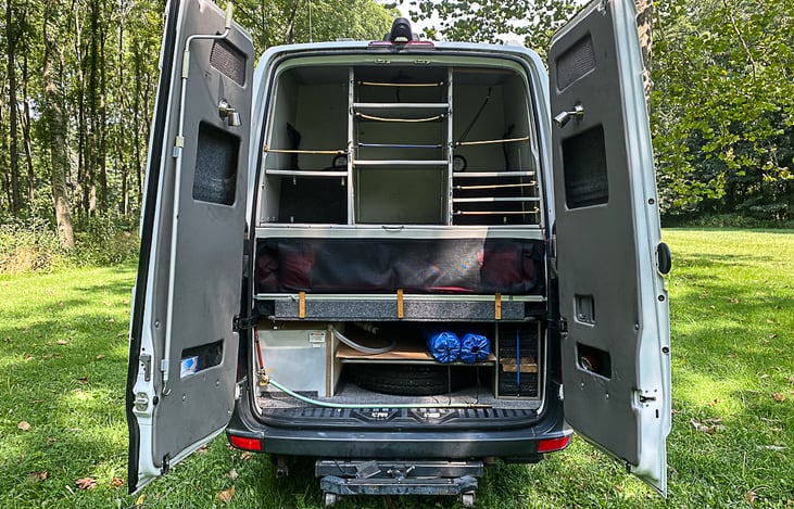 In the back, storage above, foot of bed in center, and below is water tank on left, spare tire in center, and leveling blocks on the right.