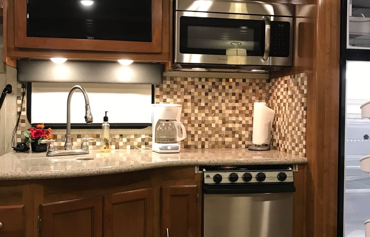 Kitchen with double sinks gas stove and oven, microwave and refrigerator.