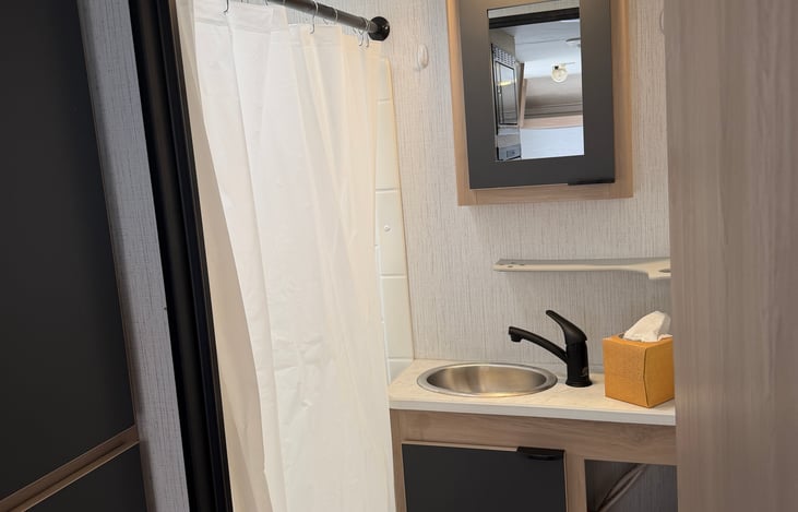 Clean and convenient private bathroom featuring a foot-flush toilet, standing shower, and dedicated storage to keep your essentials organized.