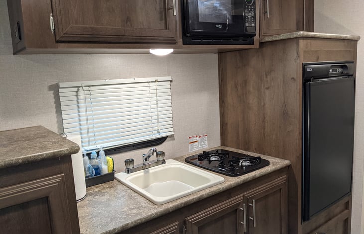 Small but mighty kitchen. Fridge works on or off-grid. Microwave only works with hook-ups. Sink with hot water. Propane cooktop. Paper towels, dish soap, hand soap, and a new sponge provided.