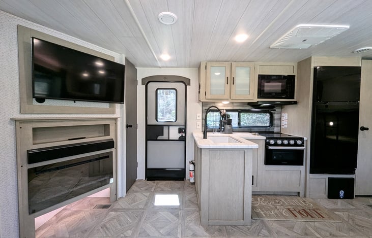 Bright and modern interior with a Custom King bed, double bunks, and a Versa-Lounge slide. Features a 30” fireplace, panoramic windows, 10.7 cu ft fridge, and a walk-in closet. Luxury camping at its f