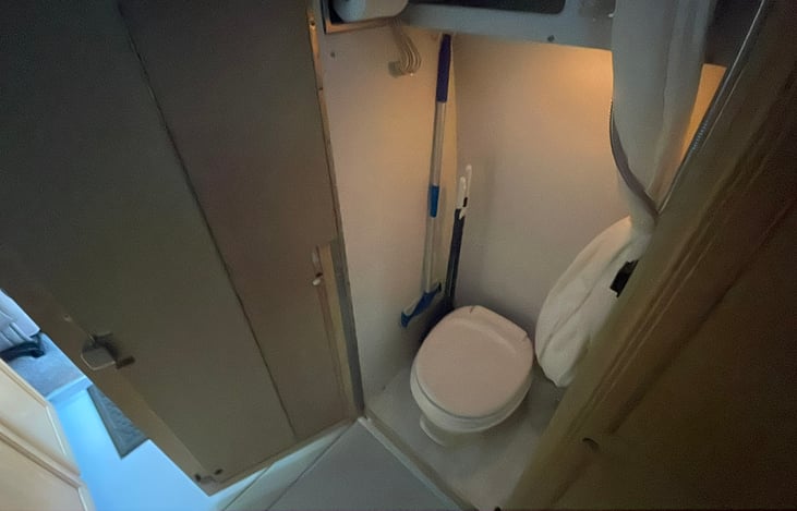 Toilet and shower are contained in the right closet. The bathroom door and closet doors fold open to provide an aisle bathroom with shower and drain. The shower curtain opens on a track in the aisle.