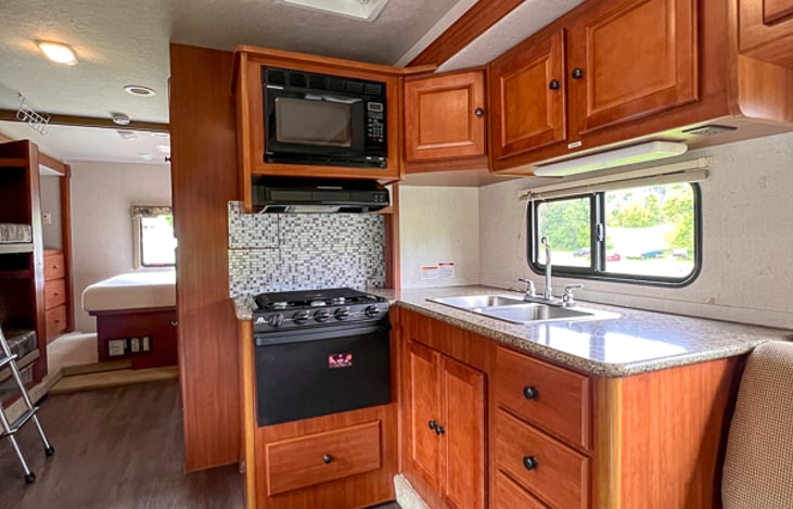 Usable kitchen space with microwave, stove top, oven, coffee maker, sink, hot water and cupboard storage.  Utilize the onboard generator and LP gas to cook anywhere, anytime.