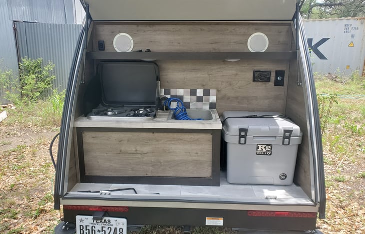 Rear outdoor kitchen area with 2 burner stove, sink/outdoor shower, K2 cooler, outlets, and speakers from the stereo inside.