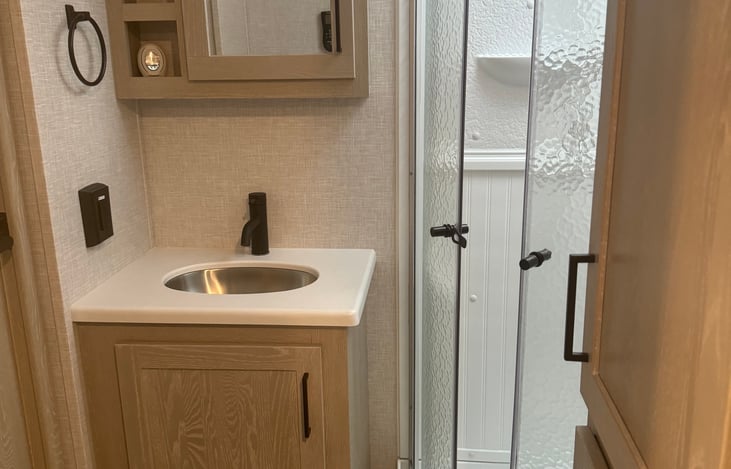 Bathroom has mirrored medicine cabinet with shelves for storage, large, walk-in shower, storage in the top covered unit. Access to bathroom from hallway and bedroom.