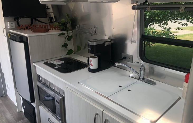 Kitchen includes fridge/freezer, microwave, stovetop, and sink. Storage provided under sink.