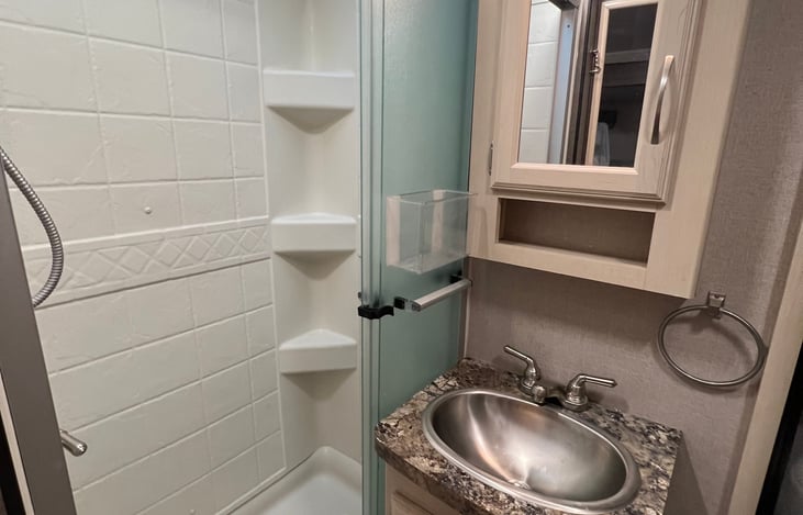 Bathroom with shower, sink vanity and medicine cabinet storage. Shower has a 13 gallon water heater (most rigs have 6 gallons) to take care of lots of people!