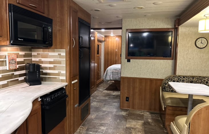 View of galley showing kitchen and fridge (left), dinette (right), living room TV and hallway leading to back suite.