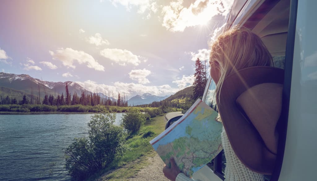 Jeune femme qui lis une carte dans un 4x4 au bord d'un lac, l'été au Canada.