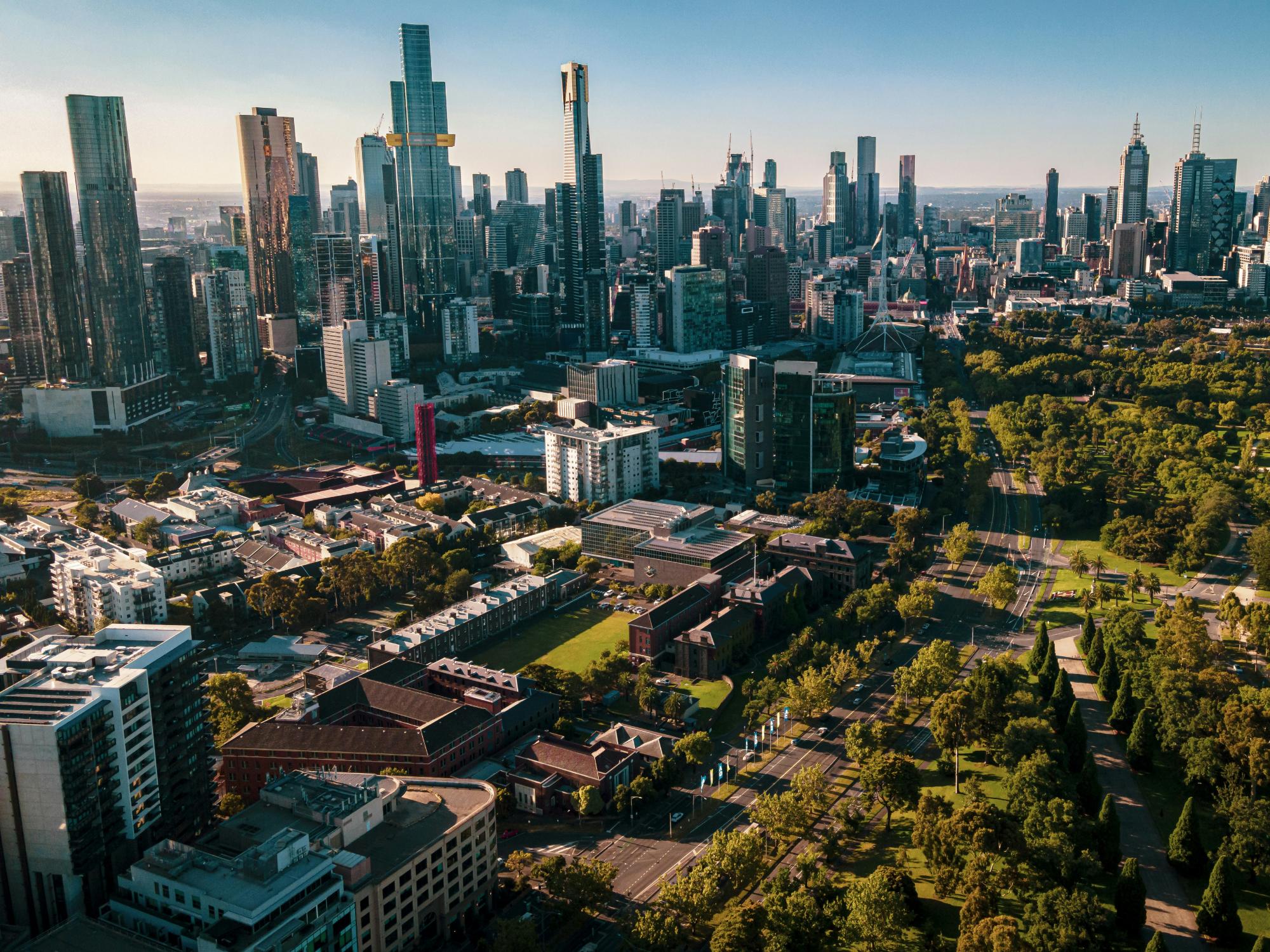 Línea de rascacielos de la ciudad de Melbourne, Australia, rodeada de parques arbolados y áreas verdes.