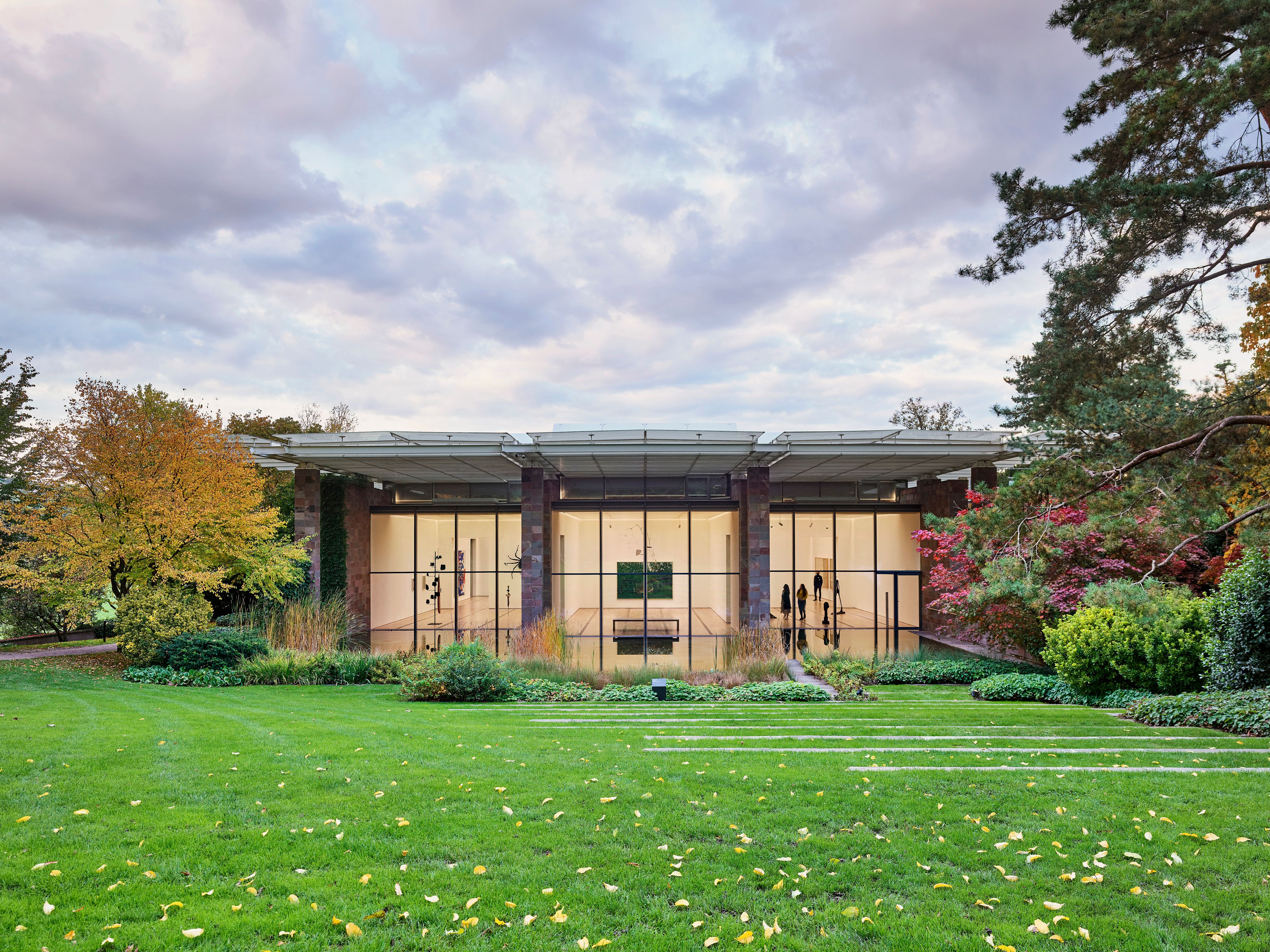 Frontansicht Musuem mit grünem Rasen, Bäume und wolkigem Himmel. Musuem und Natur.