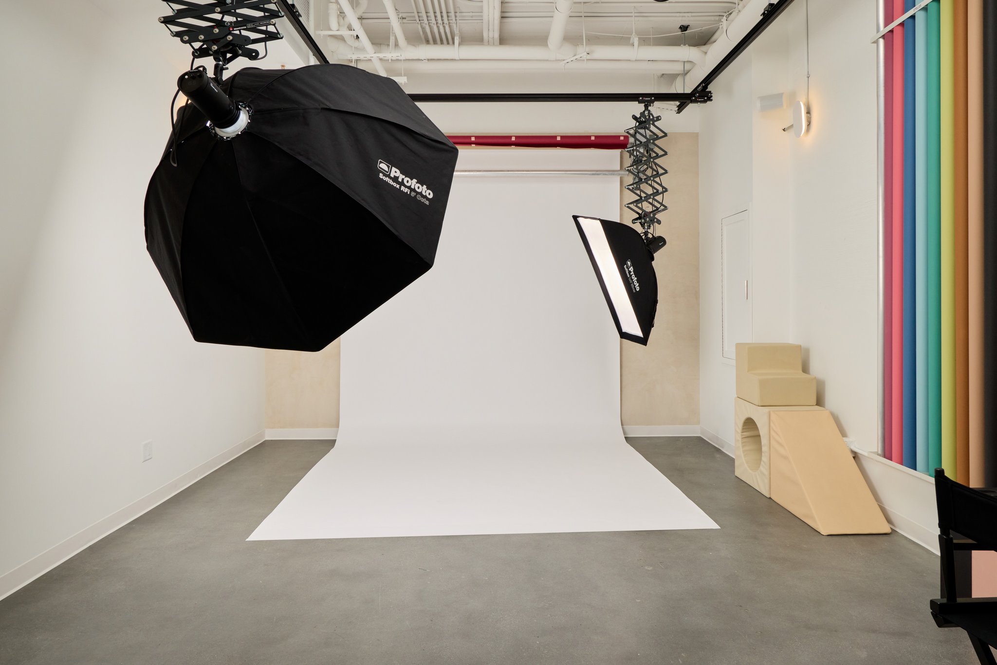 The white studio sweep under a large softbox, with posing blocks and a wall of colored backdrop rolls