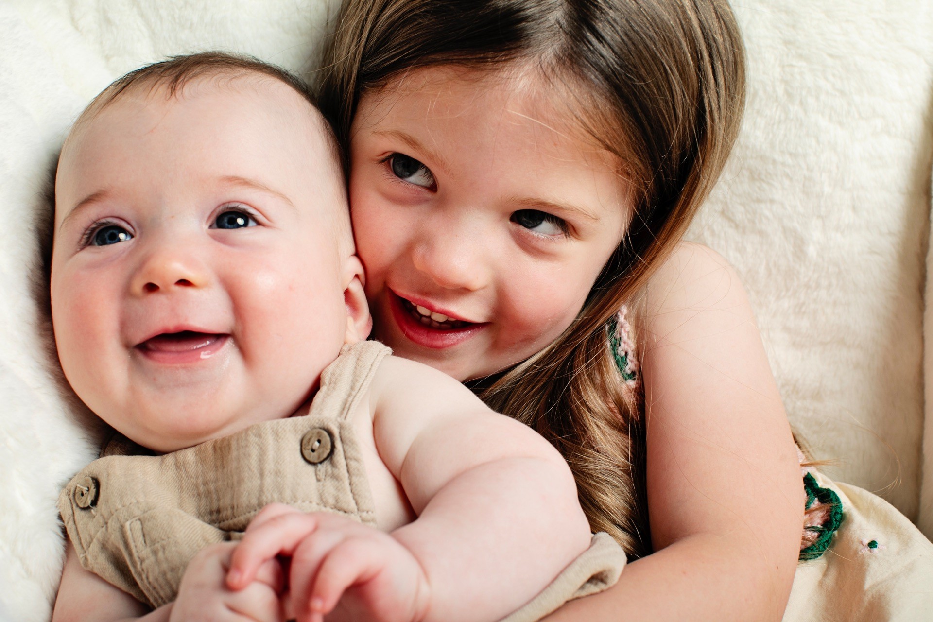 A baby and his big sister cheek to cheek, both smiling