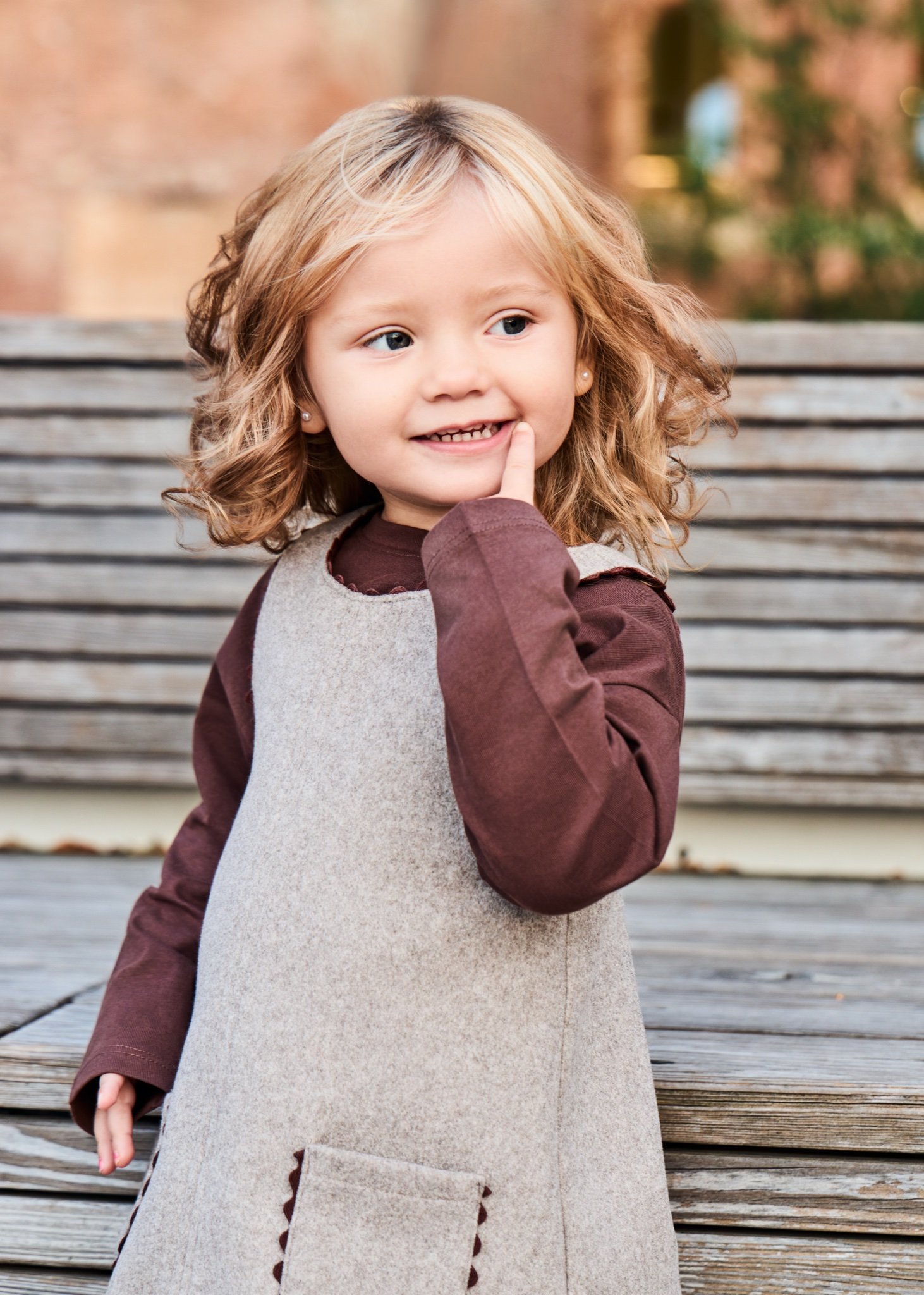 A little girl with curly hair smiling on wooden park steps