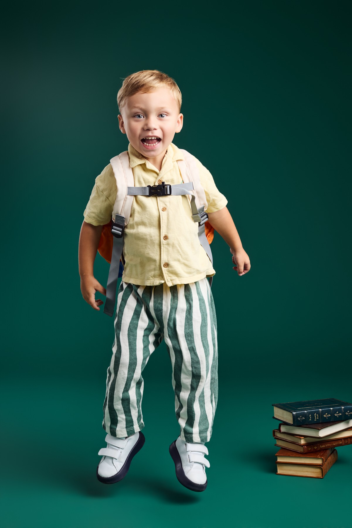A boy in a yellow shirt jumping with his backpack on